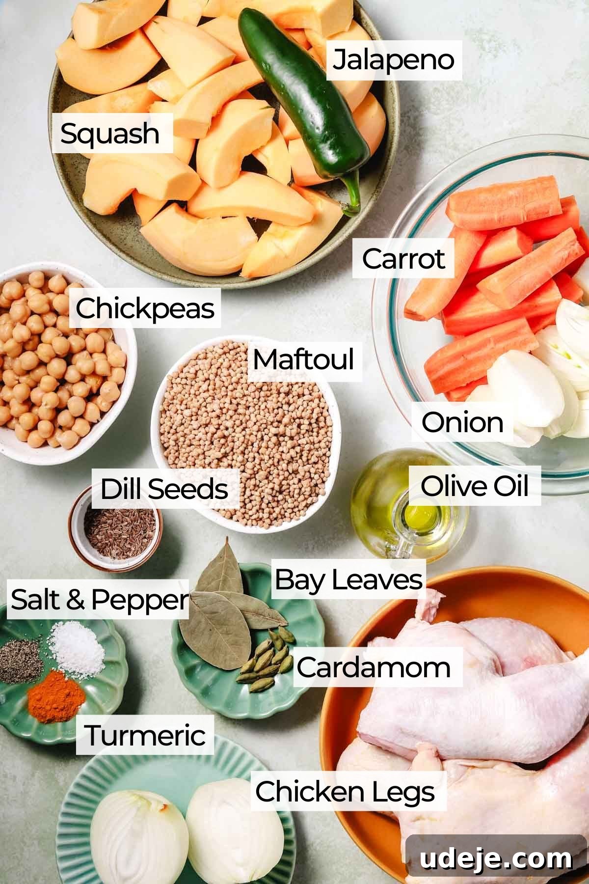 A collection of fresh ingredients laid out for Palestinian maftoul, including vibrant squash, crisp onions, slender carrots, a solitary jalapeno, ready-to-use chickpeas, raw maftoul grains, bone-in chicken pieces, aromatic bay leaves, pungent cardamom, golden turmeric, and seasoning staples like salt, pepper, and dill seeds.