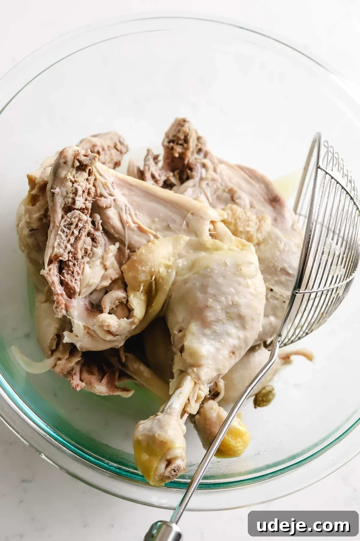 Tender, cooked bone-in and skin-on chicken legs rest in a medium glass bowl, ready to be served or further prepared, with a ladle suggesting their recent removal from a savory broth.