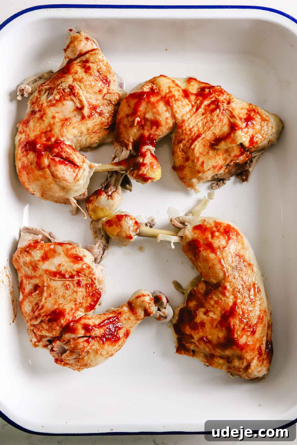 Cooked bone-in chicken legs are beautifully arranged on a baking tray, having been brushed with a rich tomato paste sauce, ready for broiling or serving.
