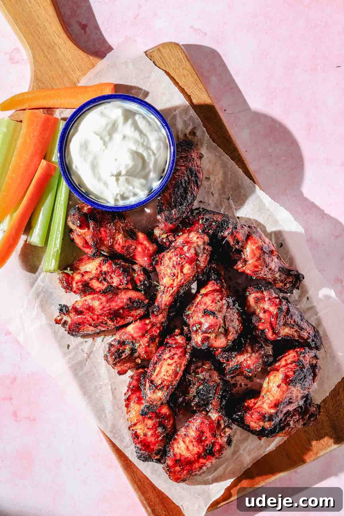 Quick Crispy Pomegranate Air Fryer Wings 2 Air fried pomegranate chicken wings on a parchment paper with carrot and celery sticks on a wooden board on a light pink background