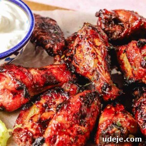 Air fried pomegranate chicken wings on a parchment paper with carrot and celery sticks on a wooden board on a light pink background