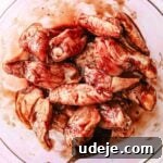 Quick Crispy Pomegranate Air Fryer Wings 5 Pomegranate sauce mixed with raw chicken wings in a glass bowl with a metal spoon on a light pink background