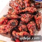 Quick Crispy Pomegranate Air Fryer Wings 7 Air fried pomegranate chicken wings on a parchment paper with carrot and celery sticks on a wooden board on a light pink background