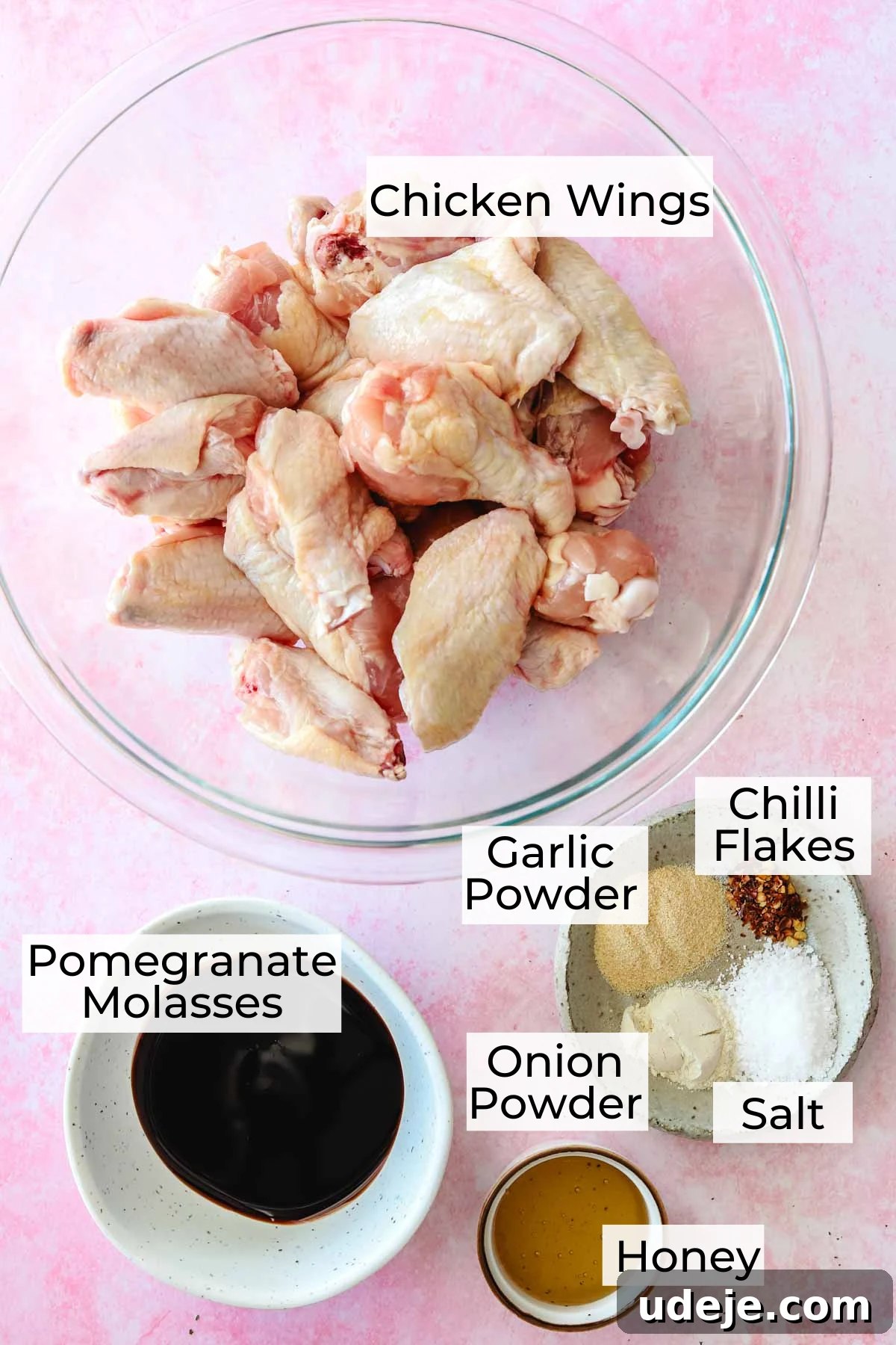 Quick Crispy Pomegranate Air Fryer Wings 3 Ingredient shot for pomegranate chicken wings with raw chicken wings in a glass bowl, a small white plate with chilli flakes, salt, garlic powder, onion powder, small white bowl with pomegranate molasses and a small white rimmed bowl with honey