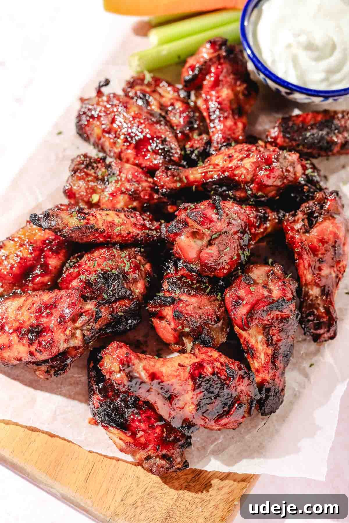Quick Crispy Pomegranate Air Fryer Wings 8 Air fried pomegranate chicken wings on a parchment paper with carrot and celery sticks on a wooden board on a light pink background