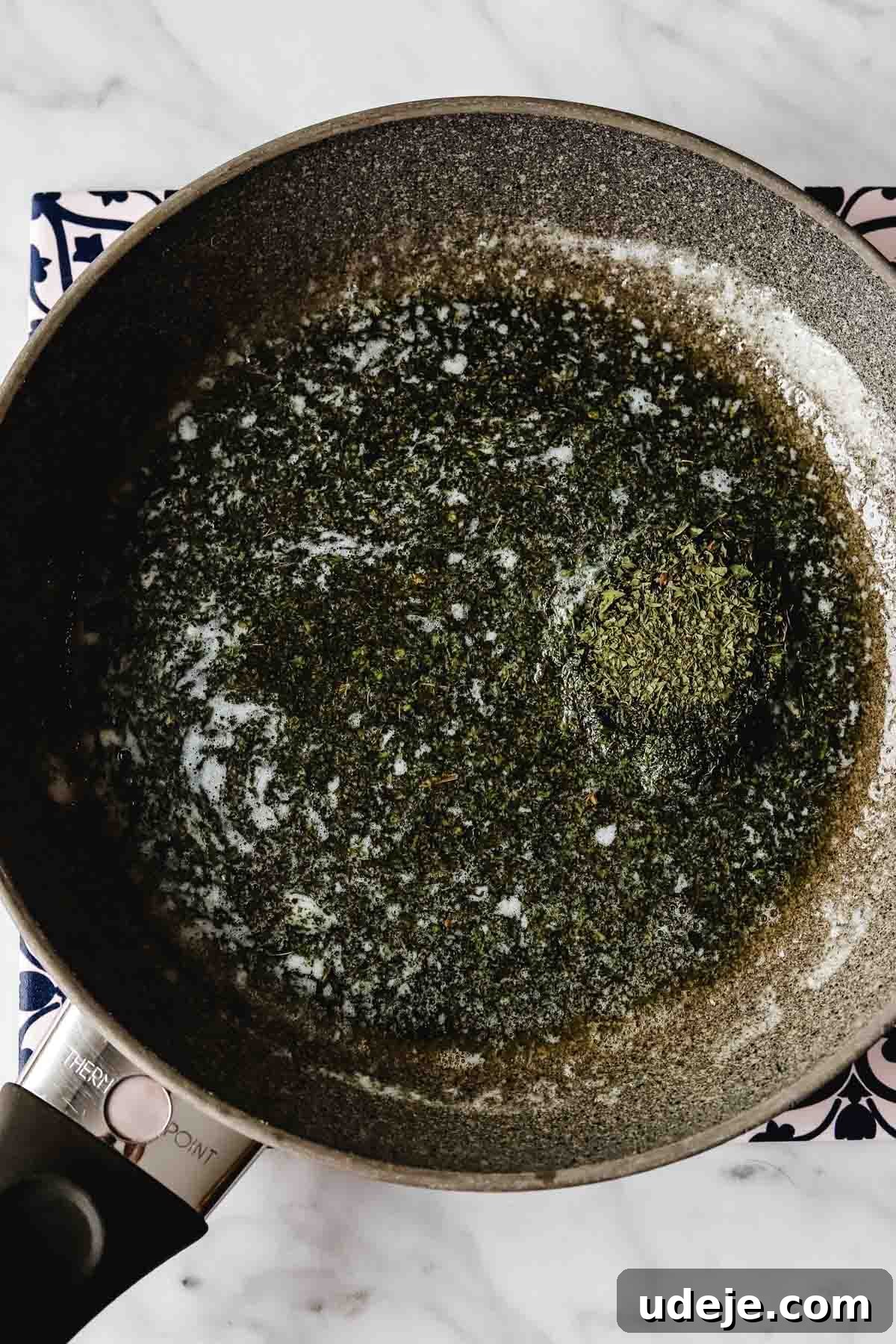 A close-up of a small non-stick skillet holding melted butter and dried mint leaves gently sizzling, releasing their aroma.
