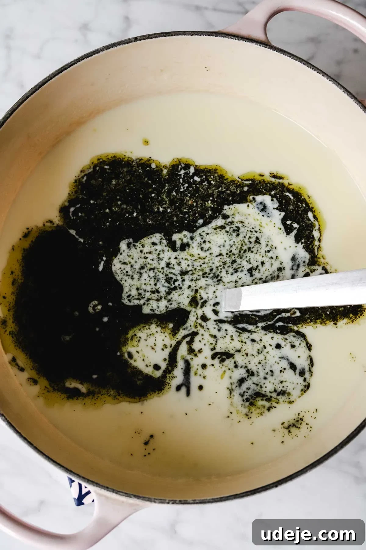 A large soup pot containing the finished Turkish yogurt soup, beautifully topped with a vibrant melted butter and dried mint drizzle, with a serving spoon resting within.