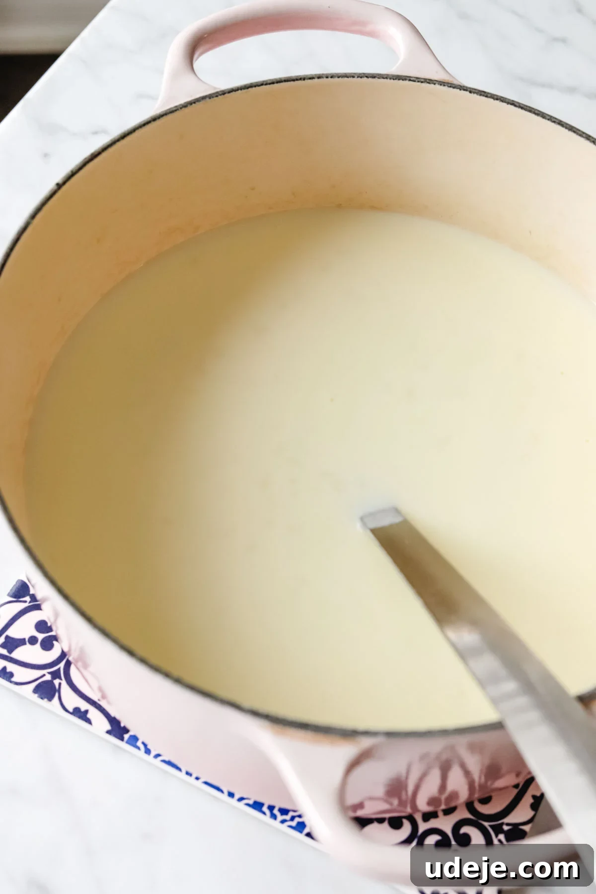 A large soup pot brimming with creamy Turkish yogurt soup, featuring a prominent serving spoon within, ready to be dished out.