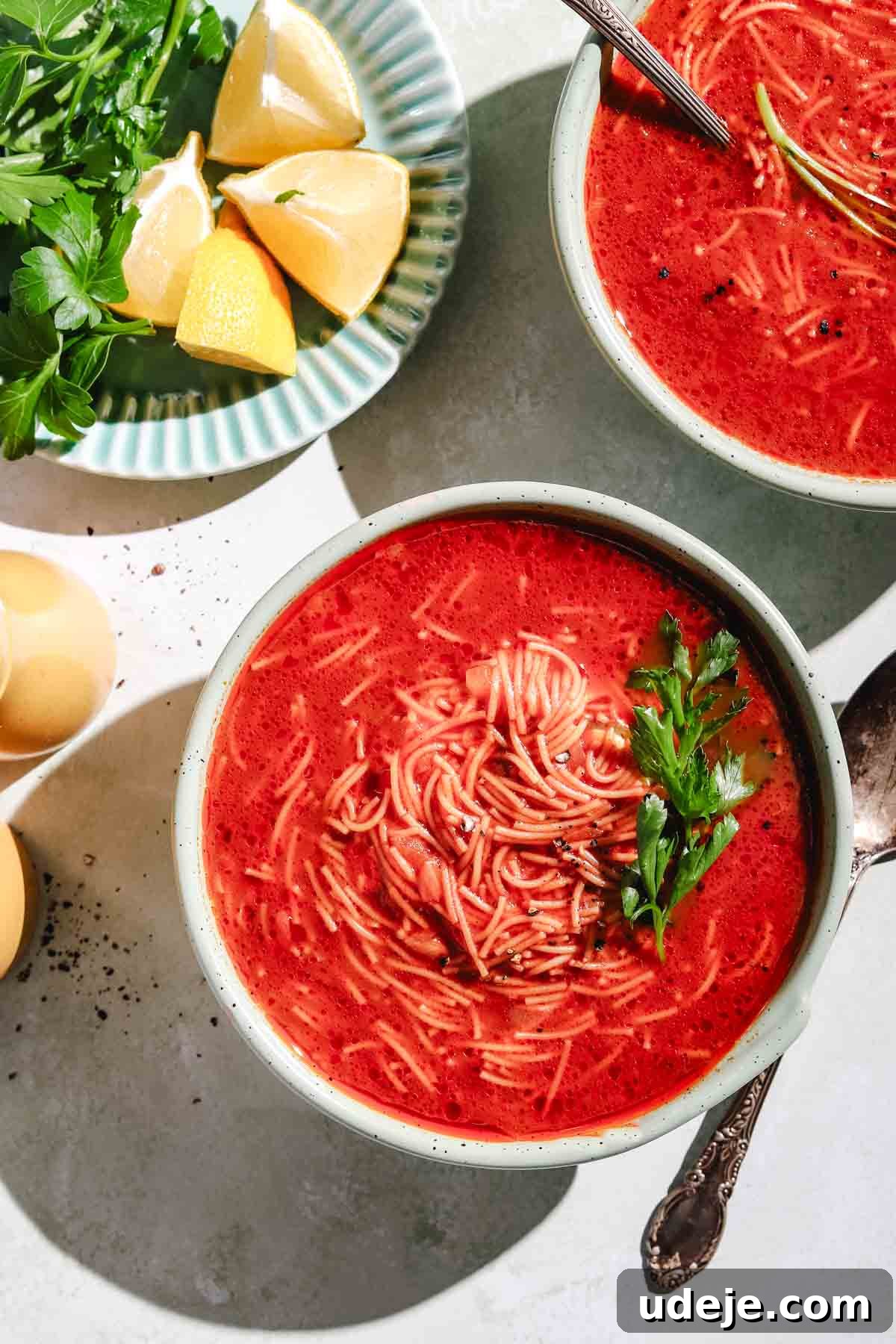 Quick Tomato Vermicelli Delight 2 Two bowls of inviting tomato vermicelli soup, artfully garnished with fresh parsley and a sprinkle of cracked black pepper. A side plate offers bright lemon wedges and more parsley for a burst of freshness.