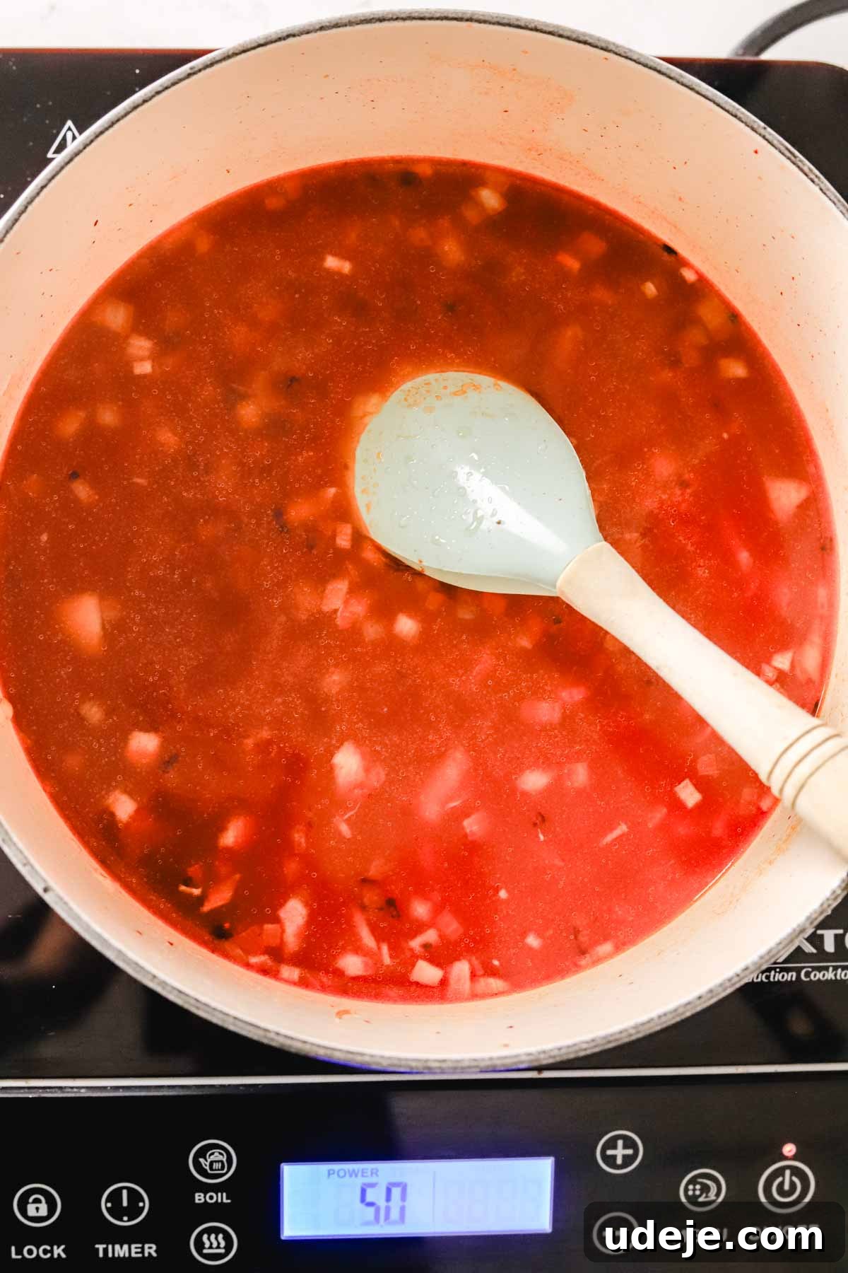 Quick Tomato Vermicelli Delight 7 A rich tomato soup, infused with finely chopped onions, simmers gently in a soup pot, stirred by a spatula on an induction stove, showcasing the vibrant base.