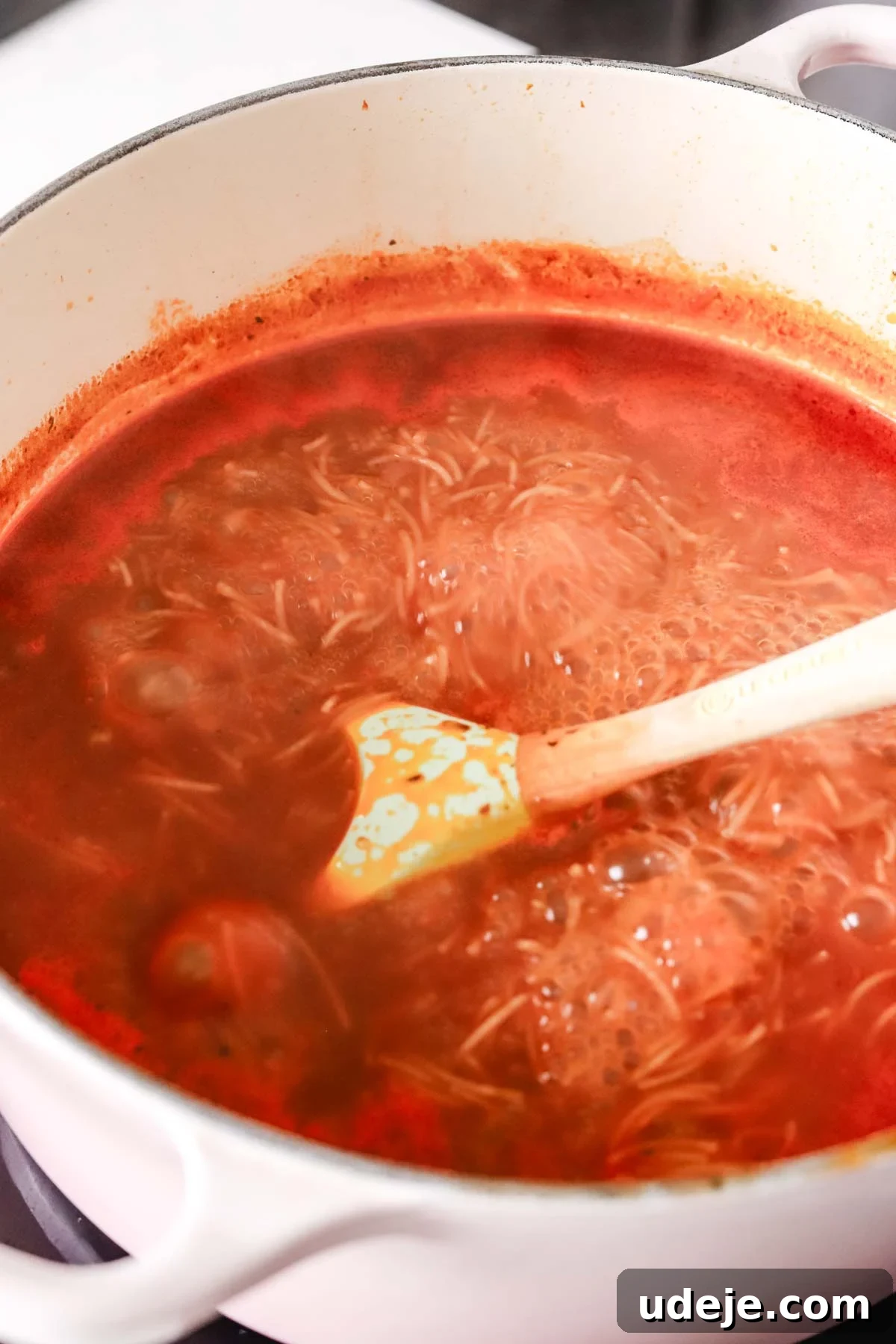 Quick Tomato Vermicelli Delight 8 A close-up of tomato vermicelli soup gently boiling in a soup pot, with a spatula resting inside, illustrating the cooking process.