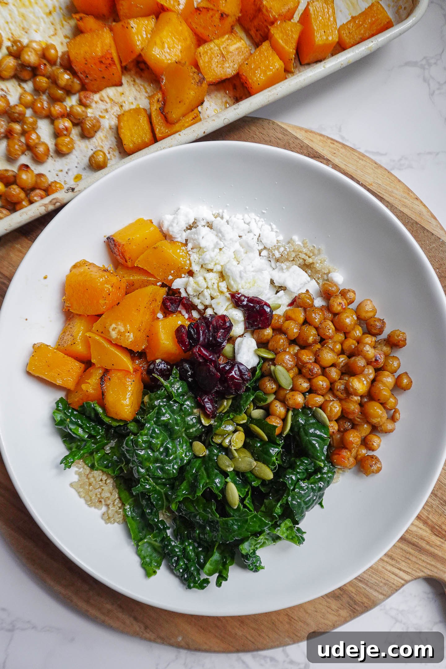 Nourishing Vegan Butternut Squash and Kale Quinoa Bowl 4 Vegan butternut squash and kale quinoa bowl topped with roasted chickpeas, vegan feta, pepitas, and dried cranberries in a maple Dijon vinaigrette.