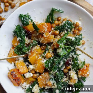 Healthy vegan butternut squash and kale quinoa bowl with pumpkin seeds, dried cranberries, and vegan feta, served with a spoon.