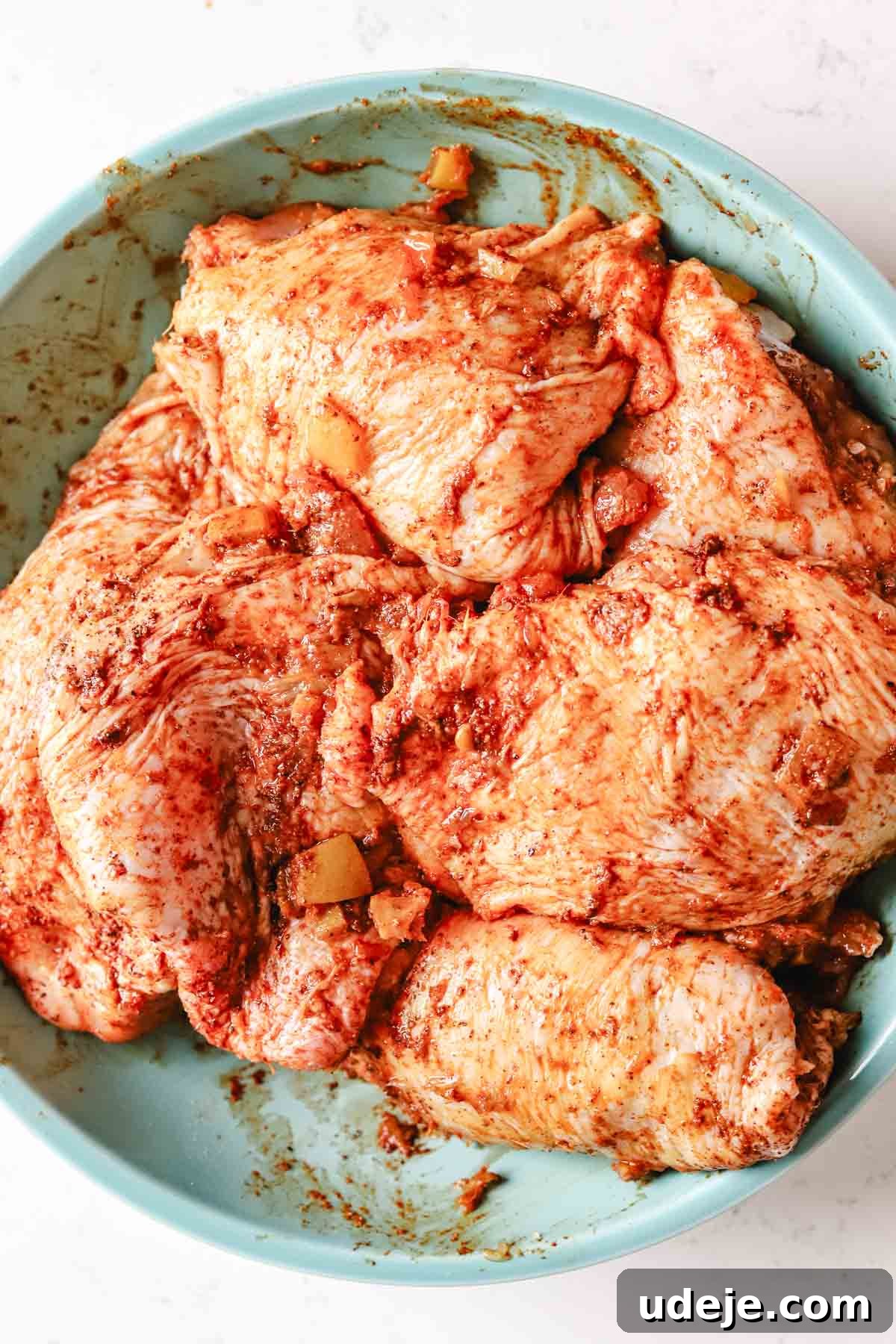 Golden Crispy Moroccan Oven Chicken 6 chicken thighs with moroccan marinade on them in a mint coloured bowl on a white marble background