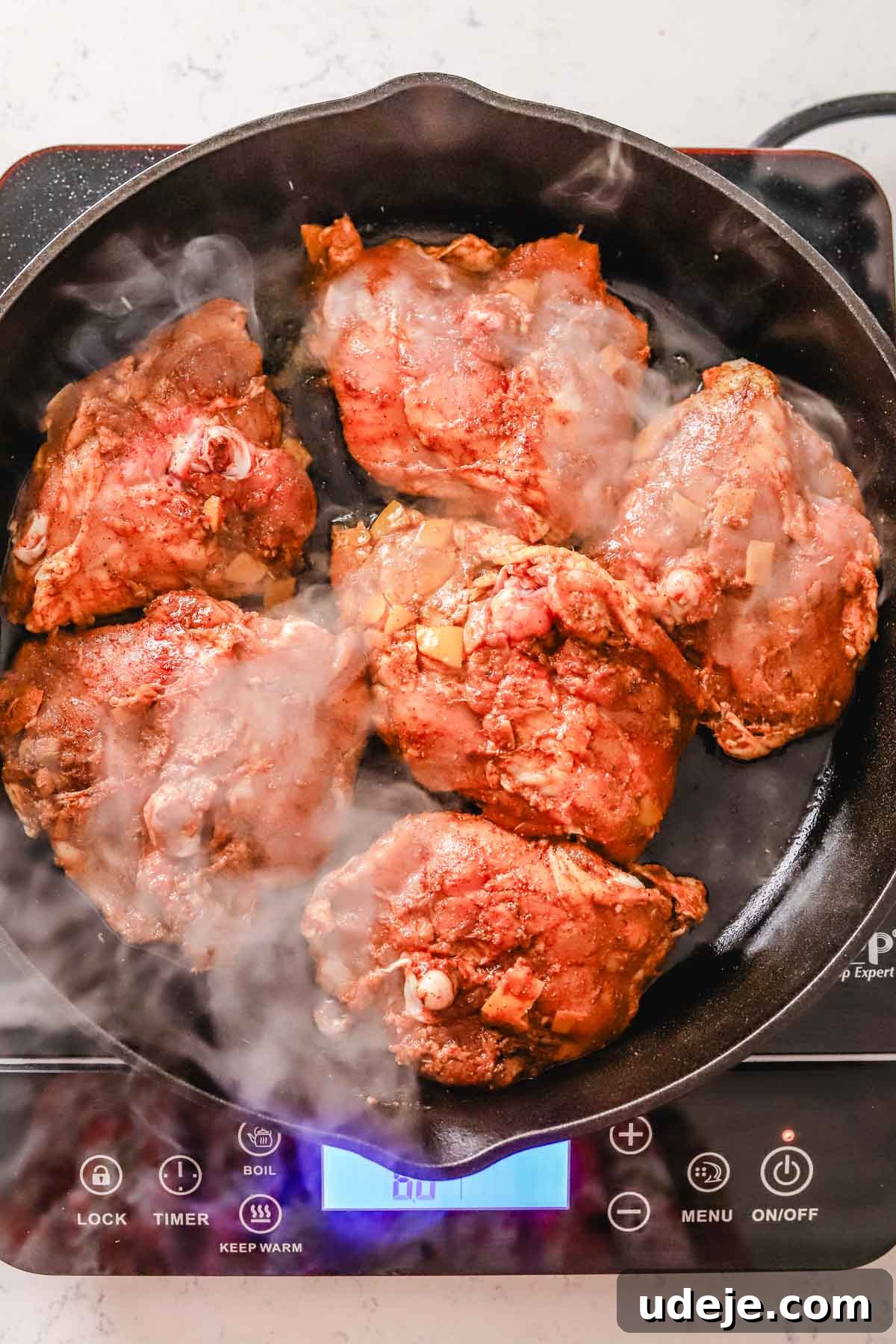 Golden Crispy Moroccan Oven Chicken 7 chicken thighs being seared in a cast iron pan on a hot plate on a white marble background