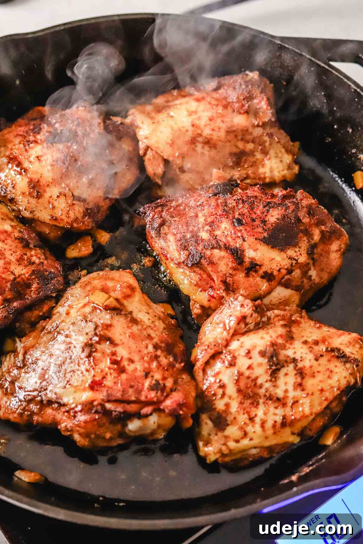 Golden Crispy Moroccan Oven Chicken 9 chicken thighs being seared in a cast iron pan on a hot plate on a white marble background