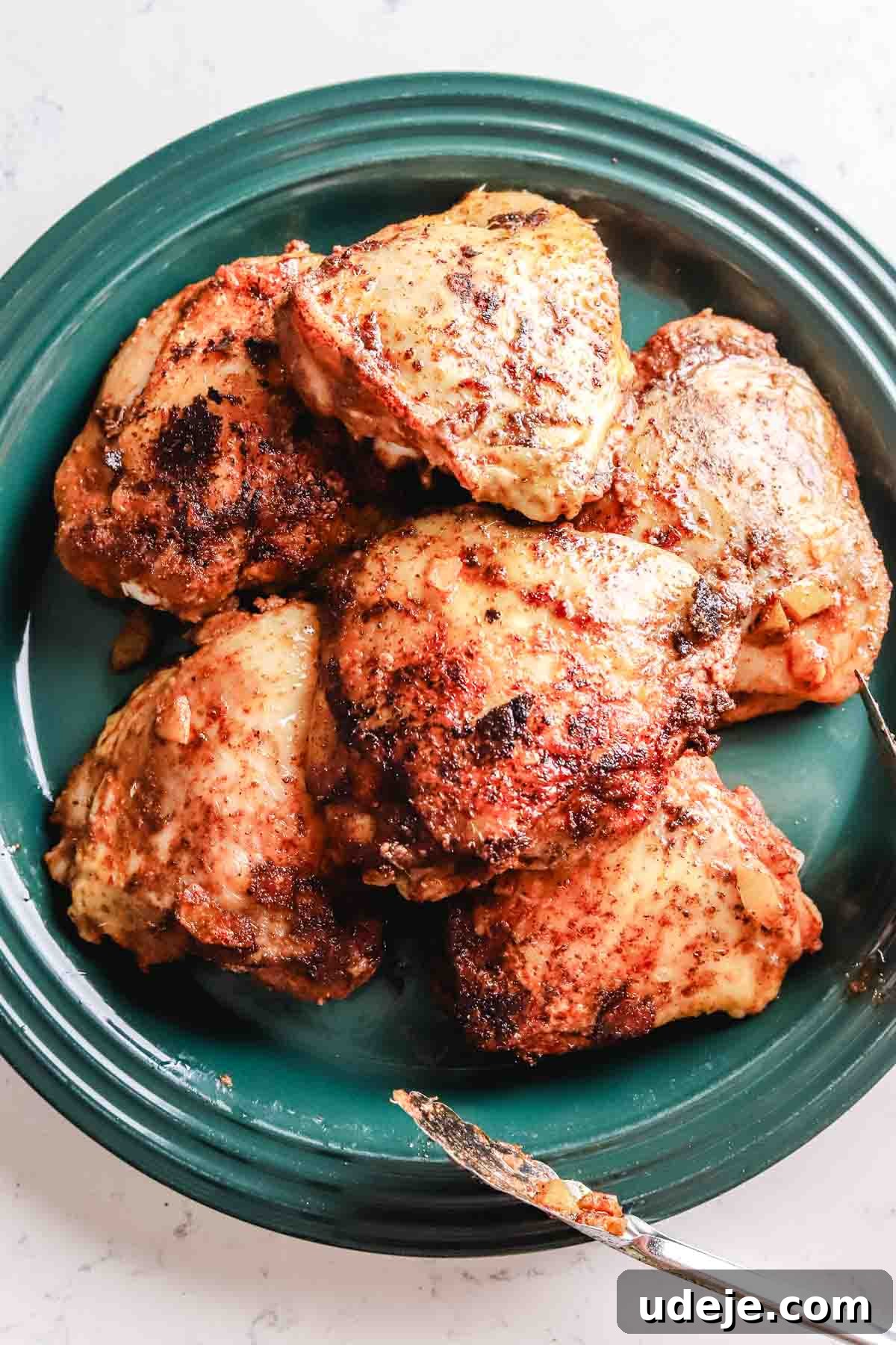 Golden Crispy Moroccan Oven Chicken 10 Seared chicken on a green plate with tongs at the side on a white marble background