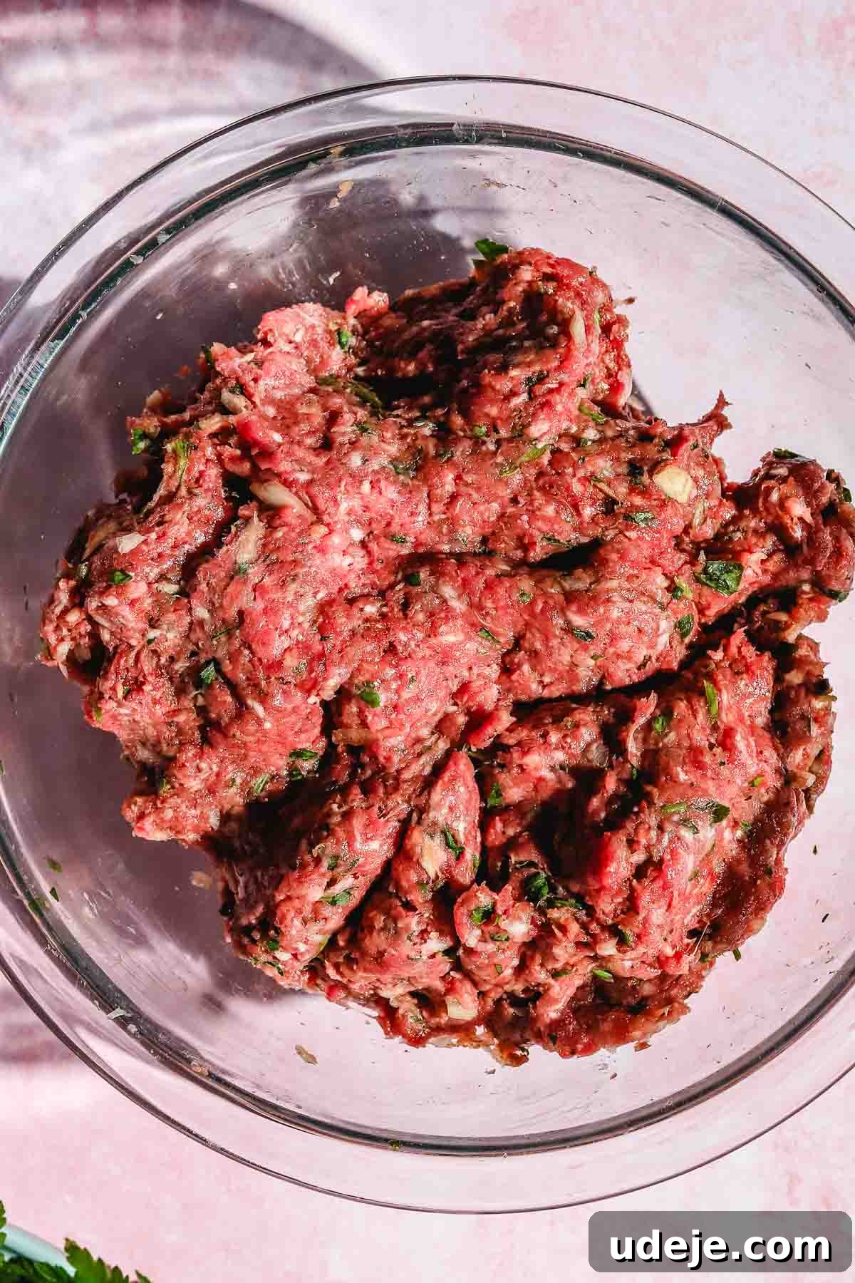 Ground beef kofta mixture in a clear glass bowl, set against a pink background.