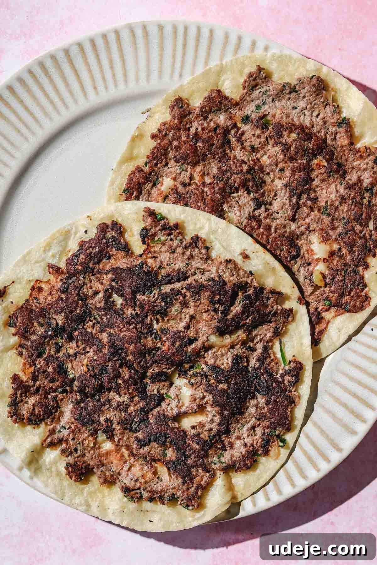 Two freshly cooked Kofta Smash Tacos, with crispy meat and golden tortillas, presented on a beige plate against a pink background.