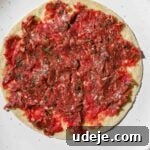 Ground beef kofta mixture spread on small tortilla on a white speckled plate on a pink background