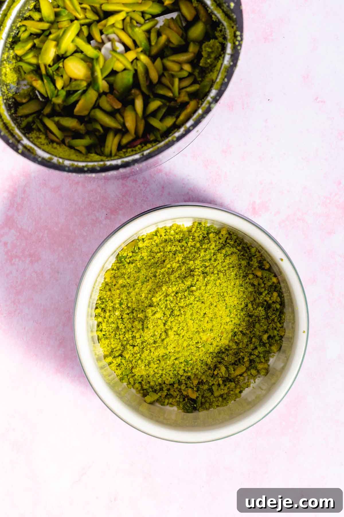 Lush Eggless Pistachio Tiramisu 16 A bowl of finely ground pistachio powder sits on a pink surface next to a container of roughly chopped pistachios, perfect ingredients for making a delicious pistachio tiramisu.