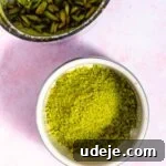Lush Eggless Pistachio Tiramisu 26 A bowl of finely ground pistachio powder sits on a pink surface, next to a container of sliced pistachios—perfect ingredients for crafting a creamy pistachio tiramisu.