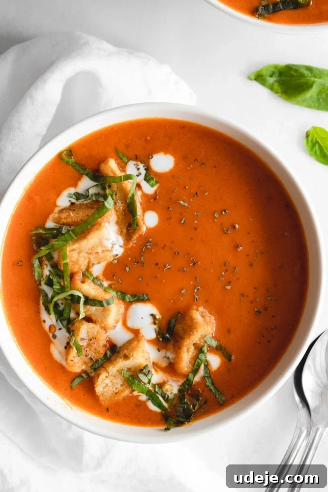 Velvety Instant Pot Roasted Red Pepper Soup 3 Close-up shot of creamy roasted red pepper soup in a bowl, garnished with a swirl of coconut cream, fresh basil leaves, and crunchy croutons.