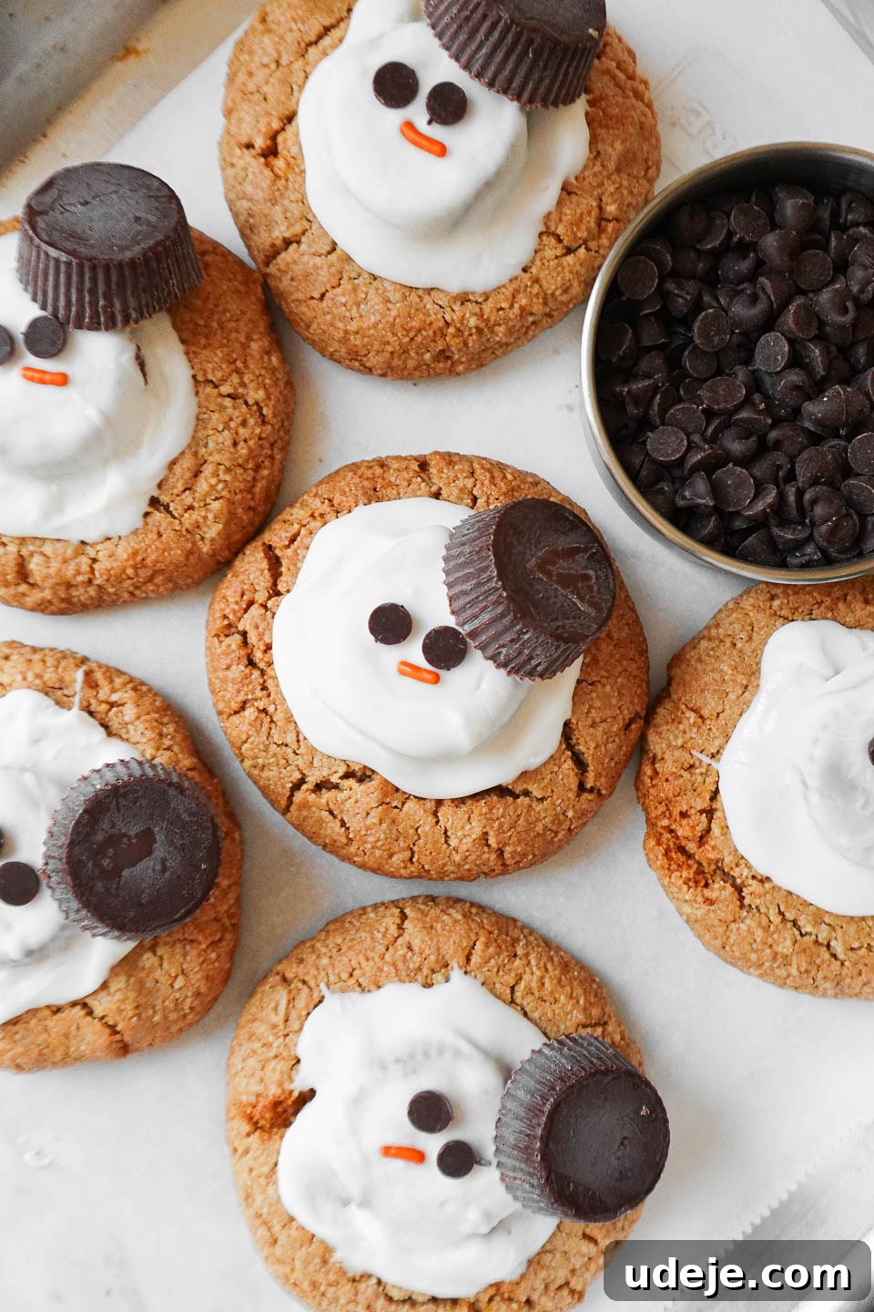 Whimsical Vegan Gluten Free Melted Snowman Cookies 5 A tray of gluten-free melted snowman cookies, each with a cheerful snowman face, topped with vegan white chocolate and mini chocolate chips for eyes and a sprinkle nose.