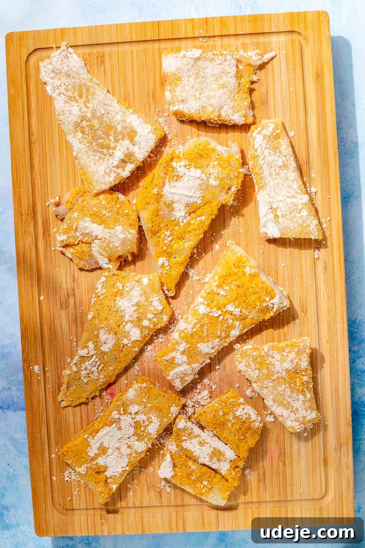 Fragrant Middle Eastern Fish Pilaf 13 Cod fillets coated with spiced cornstarch on a rectangular wooden cutting board on a blue background