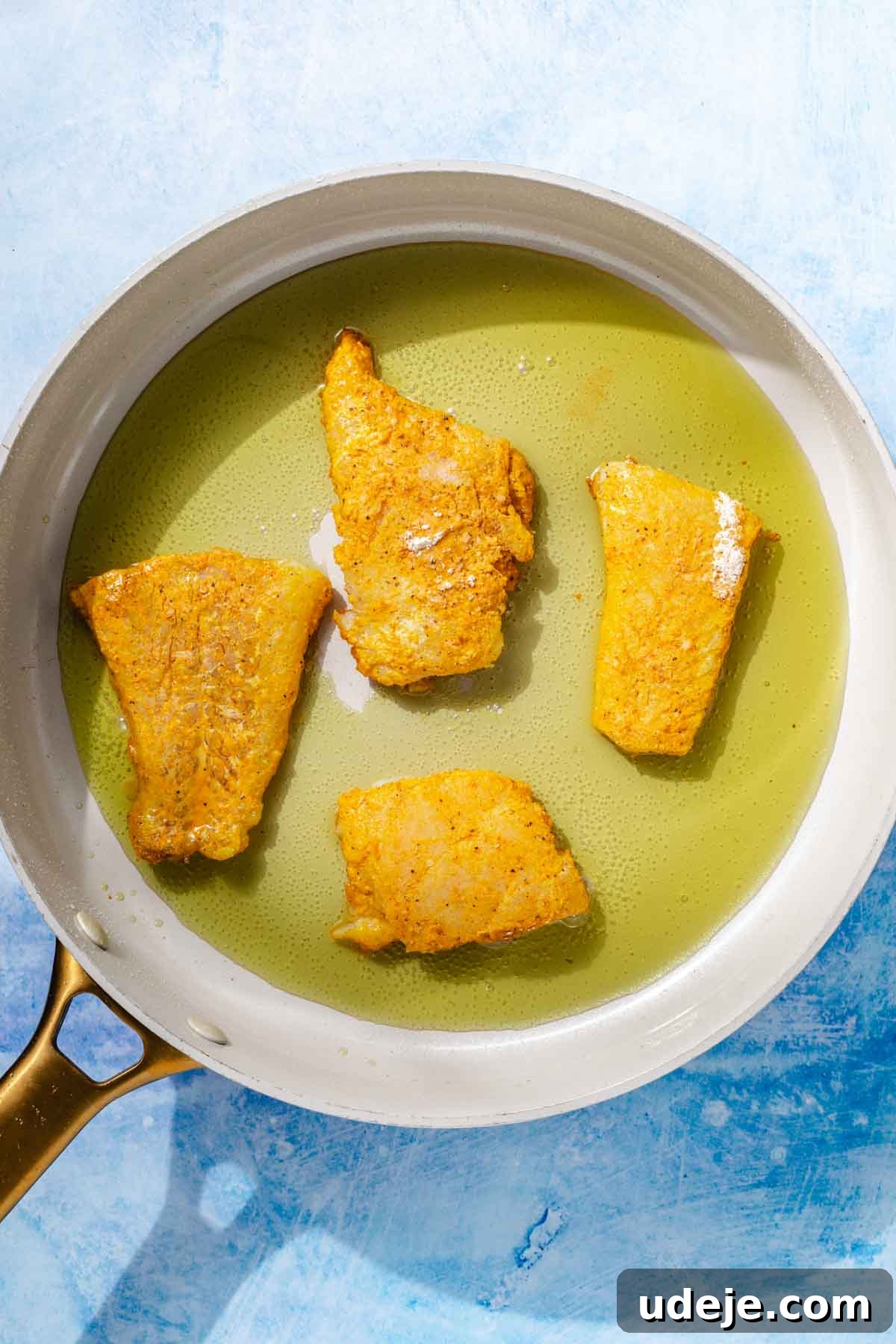 Fragrant Middle Eastern Fish Pilaf 14 Cod fillets coated in spiced cornstarch being fried in oil in a saute pan on a blue background