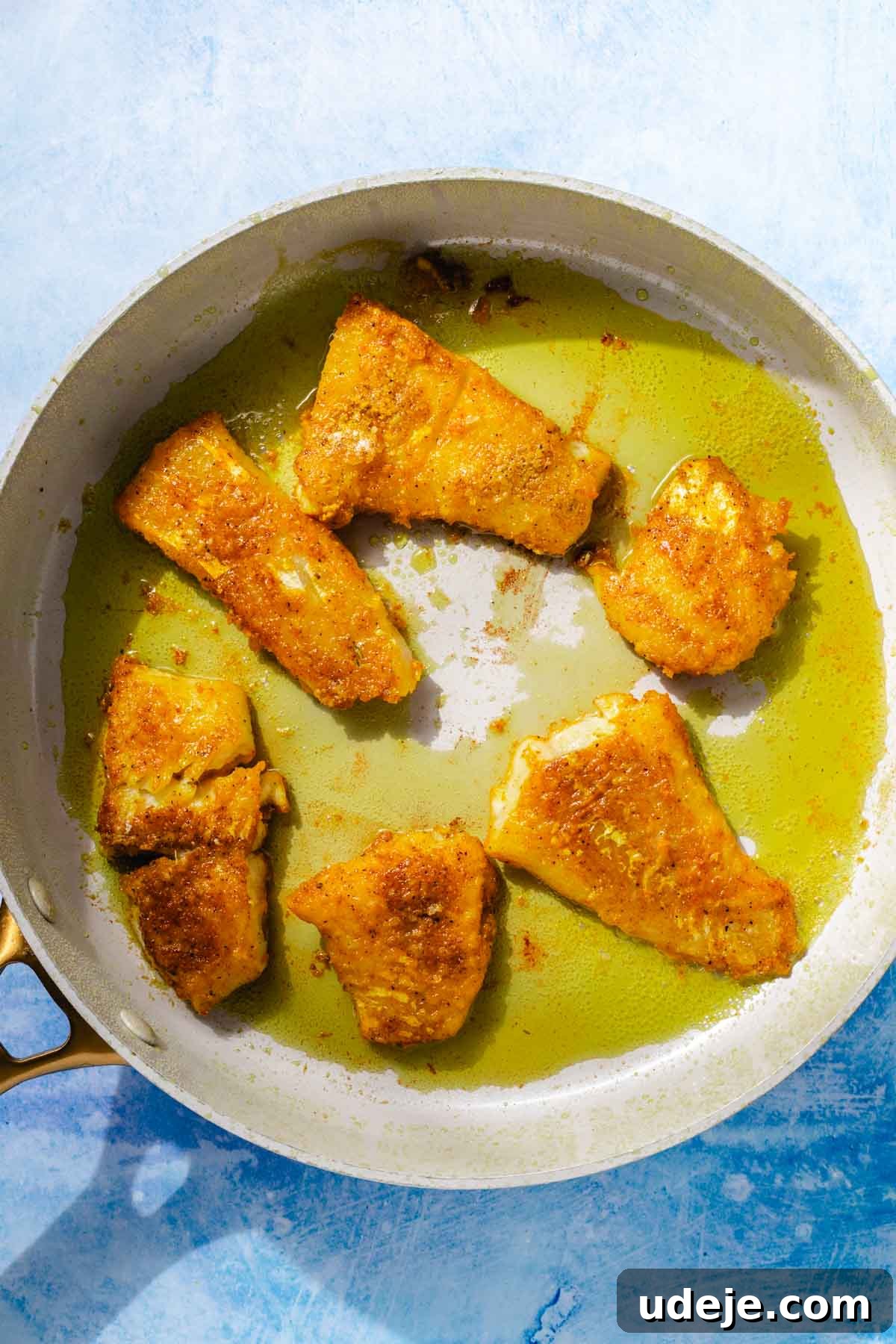 Fragrant Middle Eastern Fish Pilaf 15 Golden fried cod fillets in oil in a saute pan on a blue background