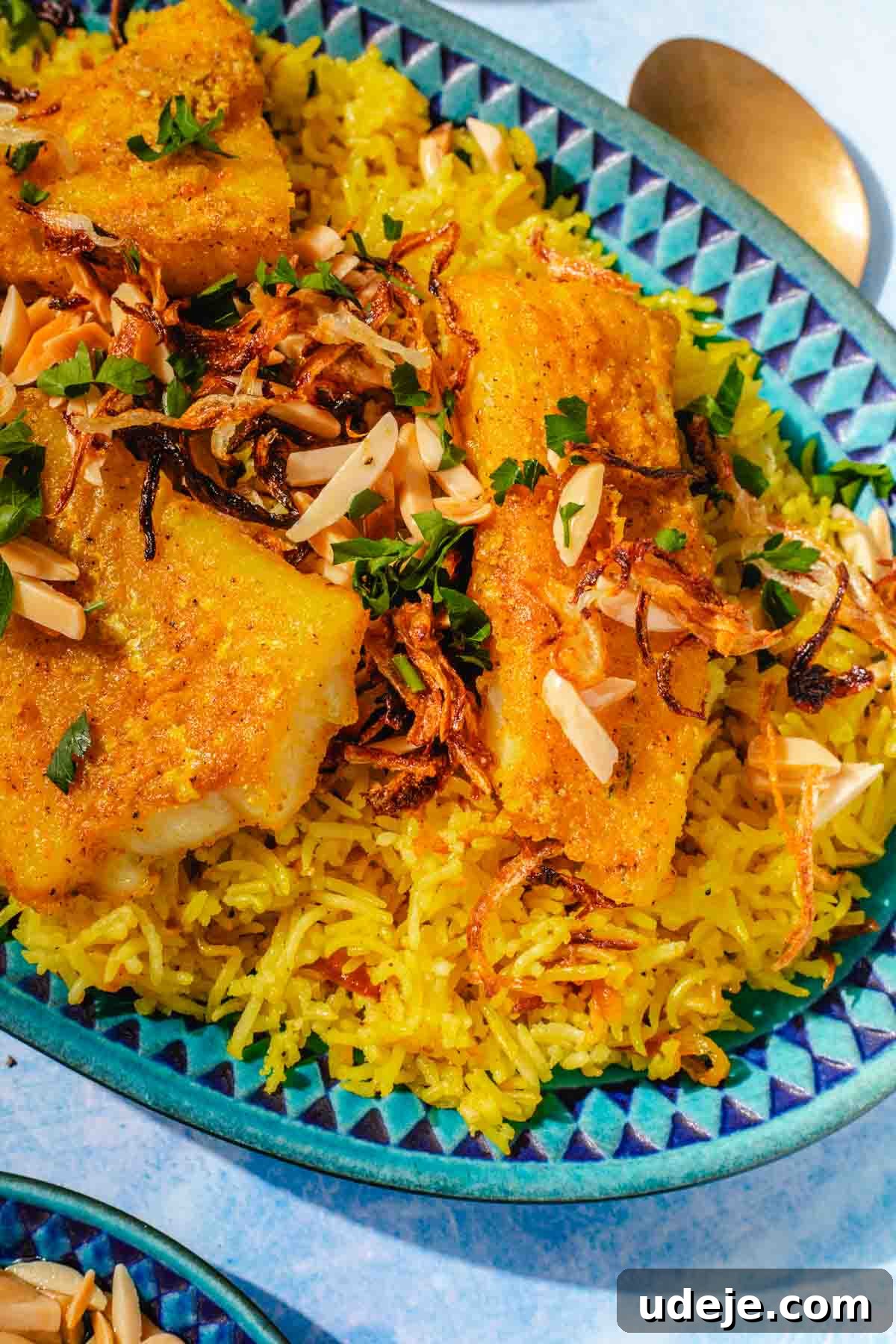 Fragrant Middle Eastern Fish Pilaf 19 Blue patterned platter with yellow rice, fried cod fillets, garnished with toasted slivered almonds, fried onions and parsley on a blue background