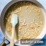 Fragrant Middle Eastern Fish Pilaf 21 Blanched slivered almonds in a saute pan with oil with a light blue spatula on a blue background