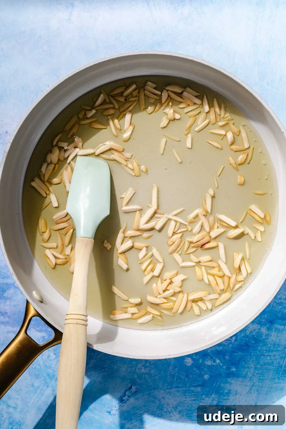 Fragrant Middle Eastern Fish Pilaf 4 Blanched slivered almonds in a saute pan with oil with a light blue spatula on a blue background