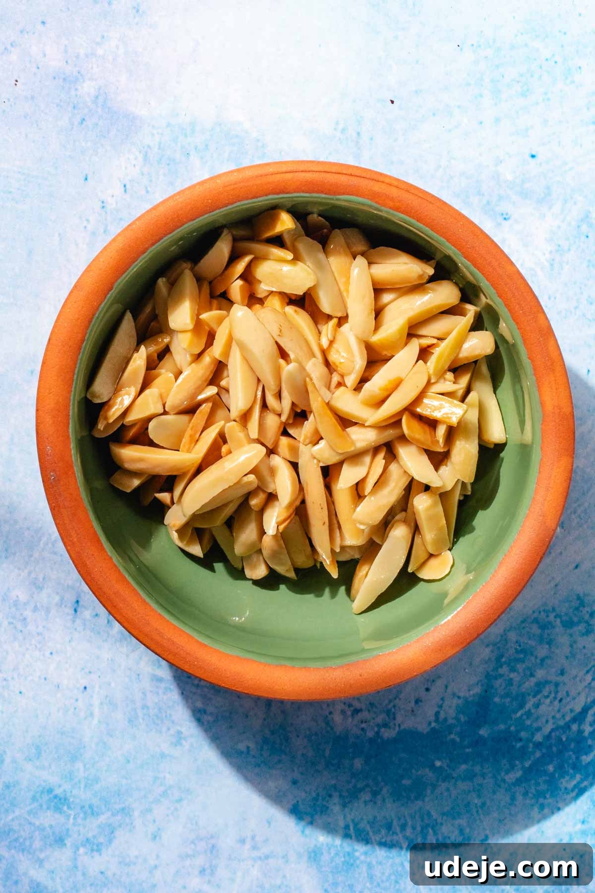 Fragrant Middle Eastern Fish Pilaf 5 Toasted slivered almonds in a green and orange rimmed bowl on a blue background