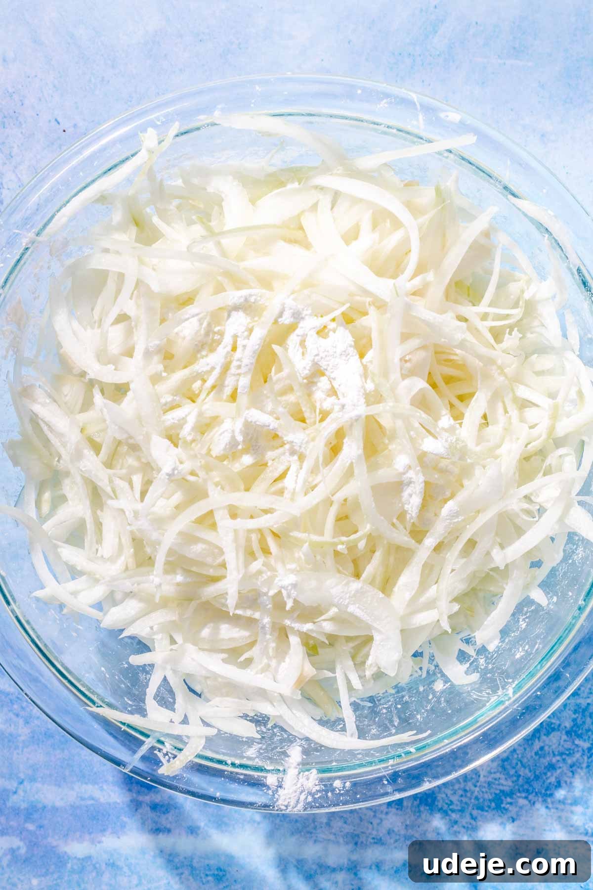 Fragrant Middle Eastern Fish Pilaf 6 Sliced onions in a glass bowl with cornstarch sprinkled on top on a blue background