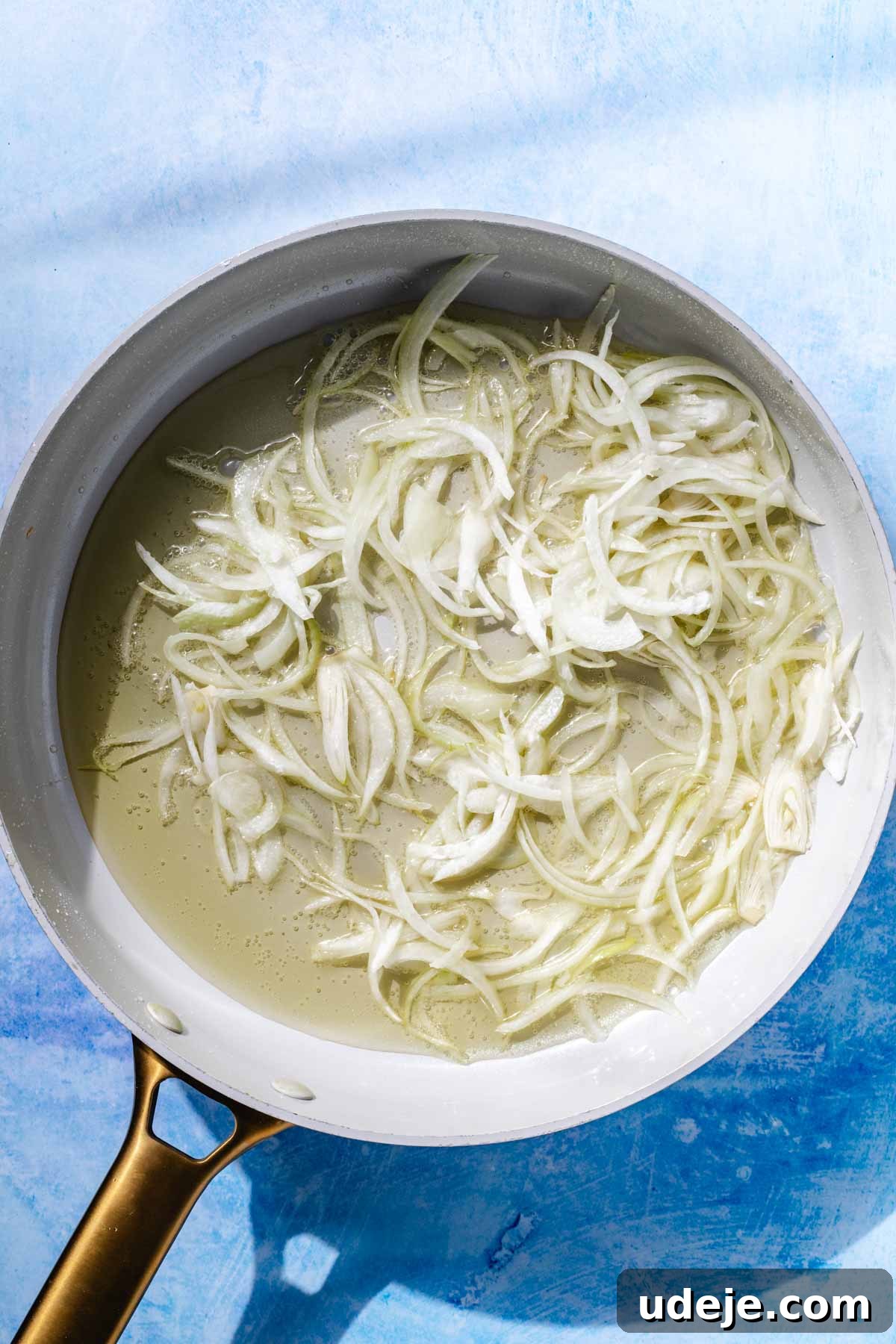 Fragrant Middle Eastern Fish Pilaf 7 Sliced onions being sautéed in a saute pan with oil on a blue background