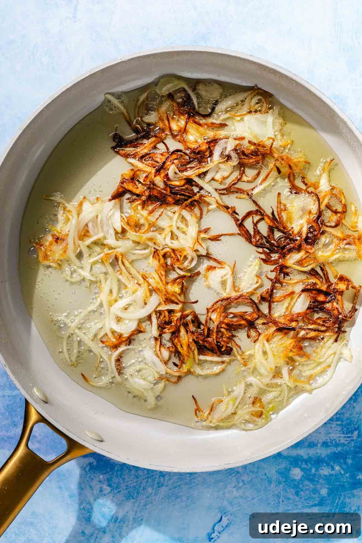 Fragrant Middle Eastern Fish Pilaf 8 Browned crispy onions in a saute pan with oil on a blue background