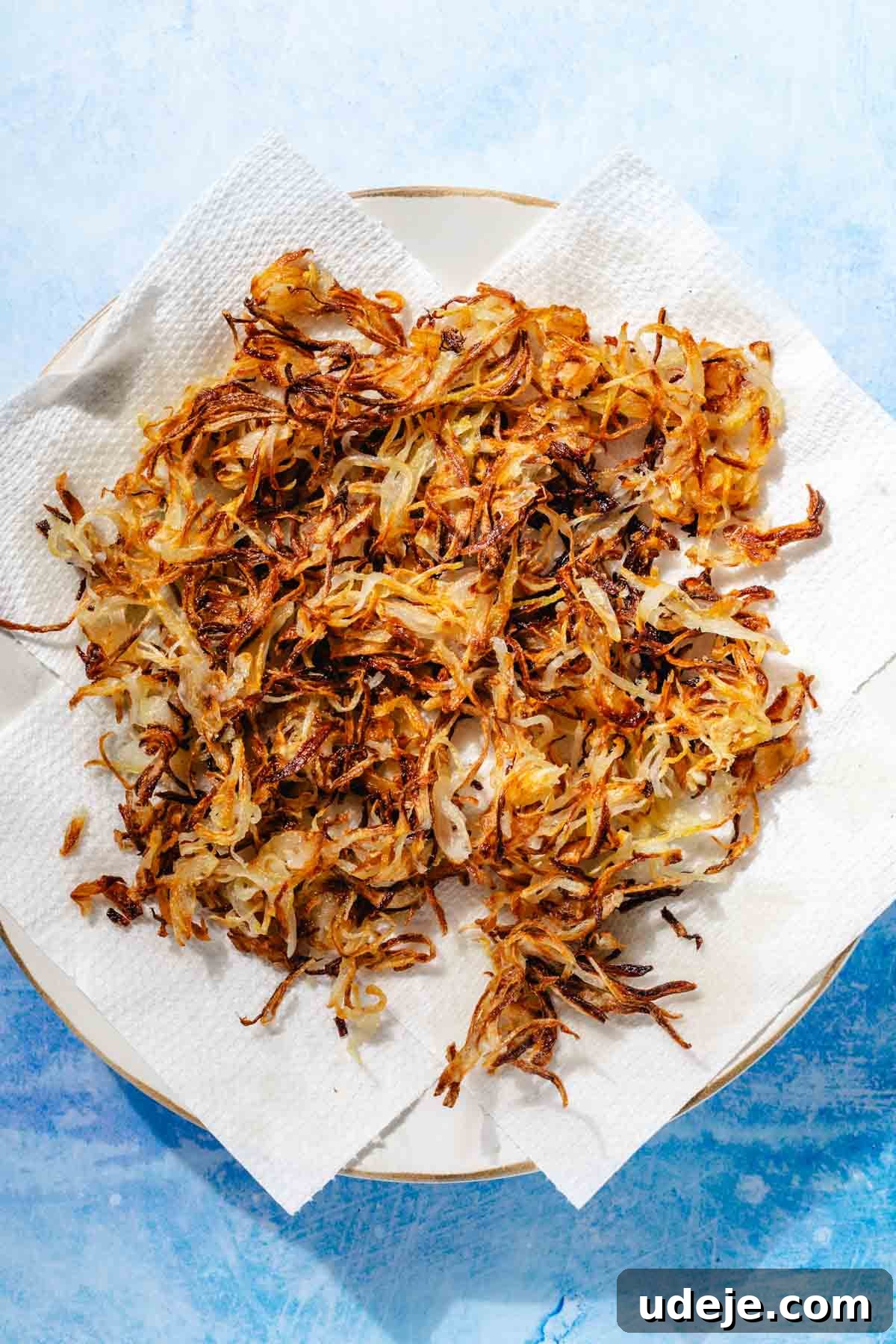 Fragrant Middle Eastern Fish Pilaf 9 Crispy fried onions on a paper towel on a gold rimmed white plate on a blue background