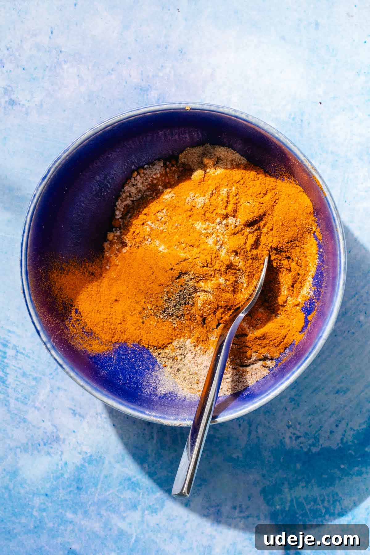 Fragrant Middle Eastern Fish Pilaf 10 Various spices mixed in a blue bowl with a metal spoon on a blue background