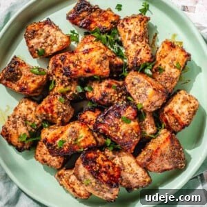 Air Fryer Salmon Bites on a light green plate, garnished with chopped parsley, beside a green tea towel on a pink terrazzo background.
