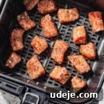 Raw marinated salmon cubes arranged in a black air fryer basket on a pink terrazzo background.