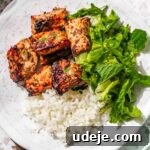 A white plate with rice, air fryer salmon bites, and fresh lettuce, perfect for a complete meal, on a pink terrazzo background.