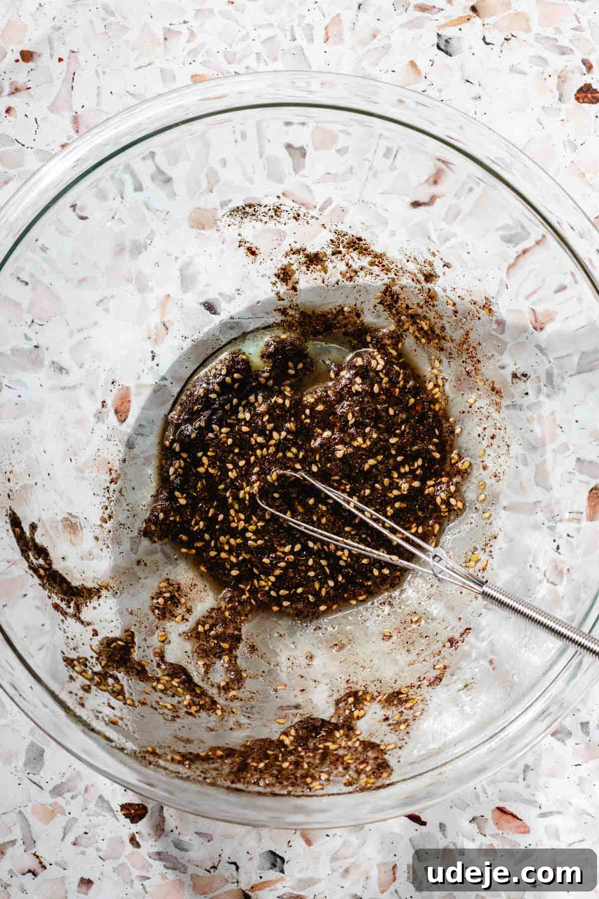 Crispy Air Fried Zaatar Salmon Bites 6 A vibrant marinade for air fryer salmon bites, freshly mixed in a glass bowl with a small whisk, resting on a pink terrazzo background.