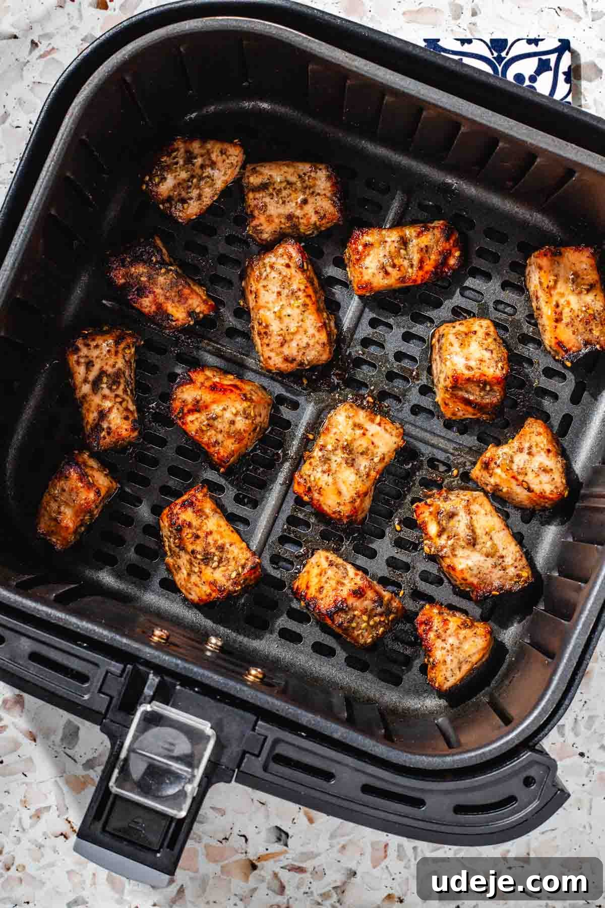 Crispy Air Fried Zaatar Salmon Bites 9 Perfectly cooked, marinated, cubed salmon glistening in a black air fryer basket, steam rising, on a pink terrazzo background.