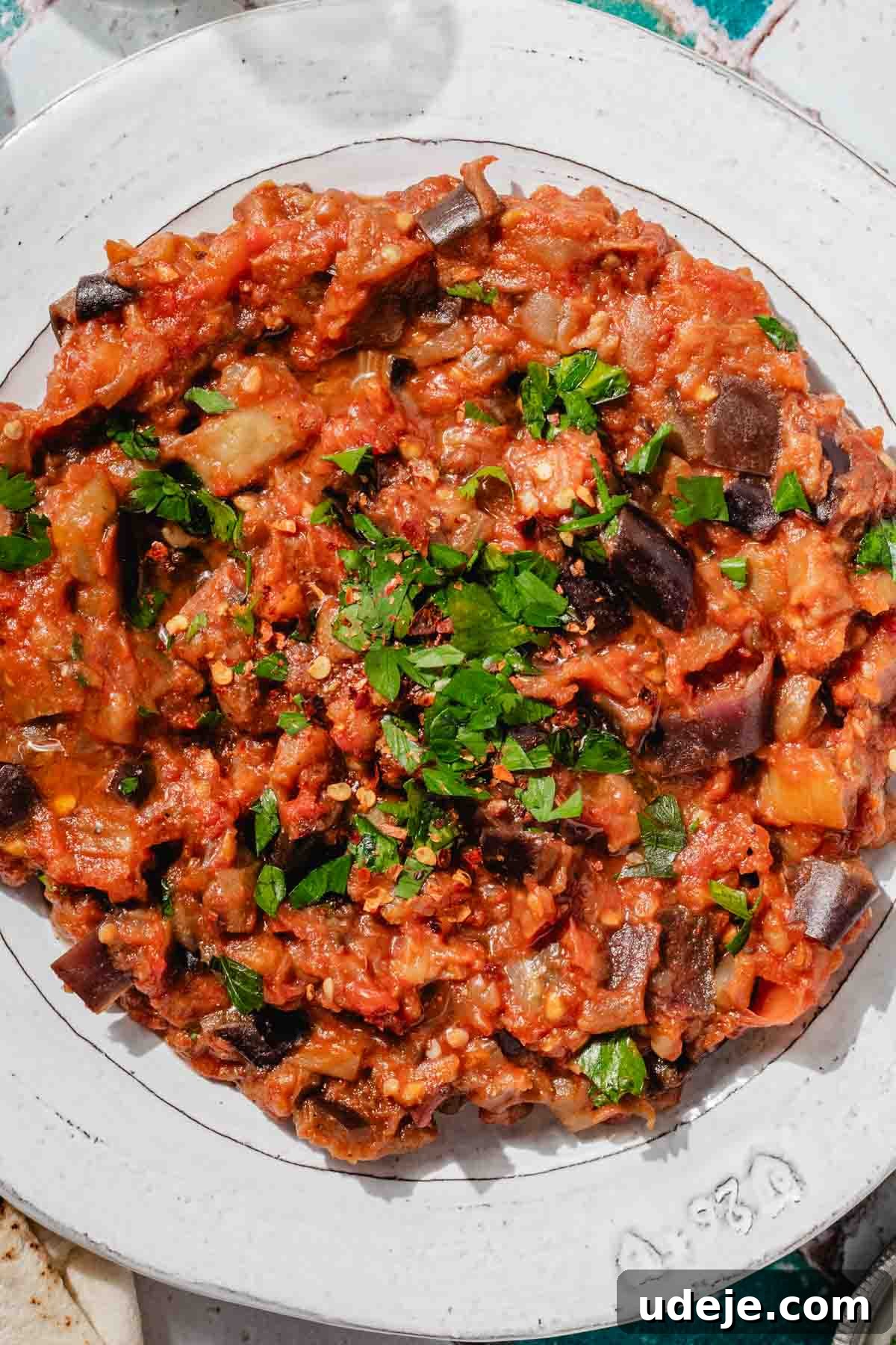 Speedy Moroccan Eggplant Zaalouk 10 Zaalouk on a white plate garnished with chopped parsley on a green and white tiled background