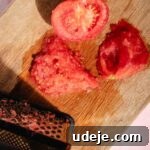 Speedy Moroccan Eggplant Zaalouk 5 Tomato cut in half in a cutting board being shredded on a metal grater on a pink background