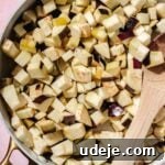 Speedy Moroccan Eggplant Zaalouk 6 Cubed eggplant in a large saute pan with a wooden spoon on a pink background