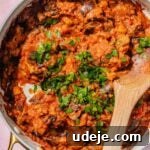 Speedy Moroccan Eggplant Zaalouk 9 Zaalouk cooked in a large saute pan with a wooden spoon and chopped parsley on a pink background