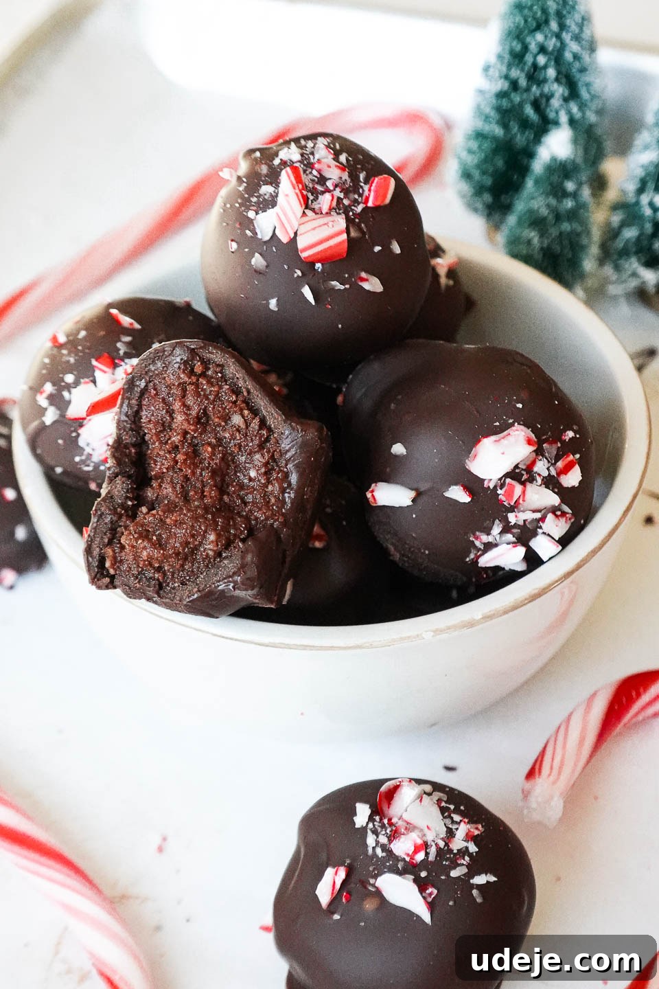Dark Chocolate Peppermint Dreams 3 Close-up of freshly made vegan chocolate peppermint truffles on a parchment-lined tray, with a glossy chocolate coating and bright crushed candy cane topping.